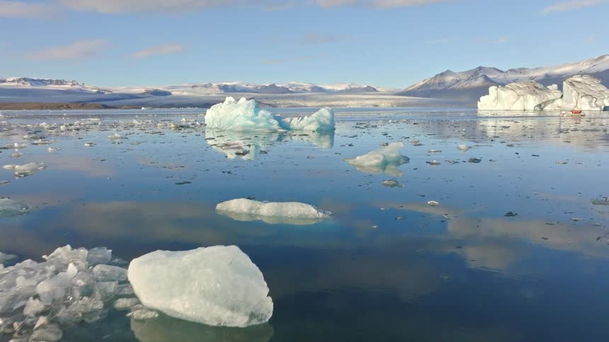 Majestic icebergs float peacefully in the calm, reflective waters of a vast glacial lagoon with snow-capped mountains in the background
