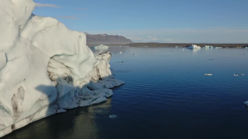 A slow aerial flight reveals majestic icebergs floating serenely in a vast glacial lagoon in Iceland