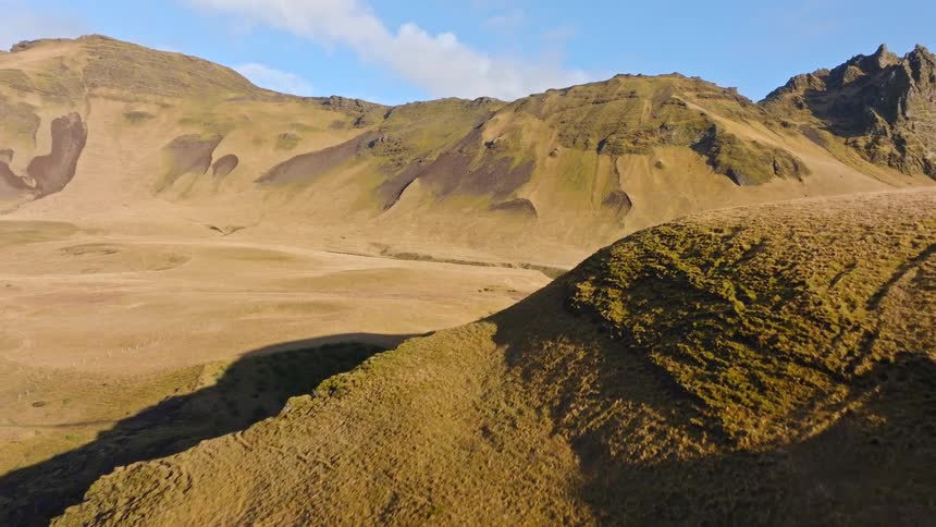A slow aerial flight reveals the vast, sun-kissed rolling hills and mountains of the Icelandic highlands