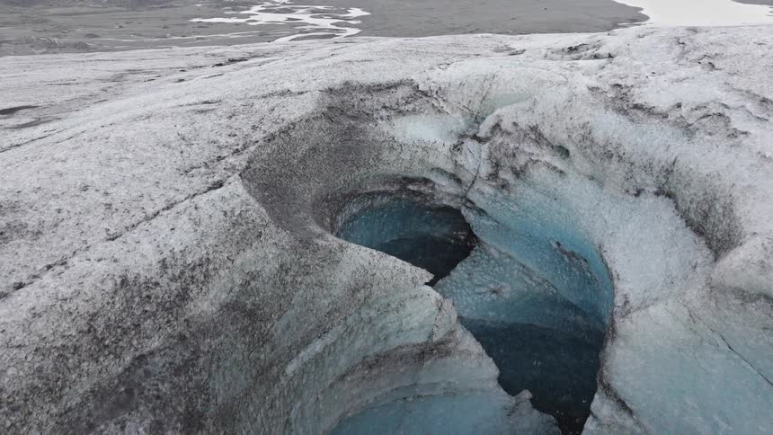 Slowly panning down from a vast glacial landscape, an aerial shot reveals a stunning blue ice canyon with a team of adventurers inside