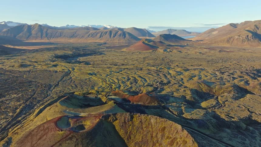 A stunning aerial pullback reveals a vast volcanic landscape with colorful craters and moss-covered lava fields in Iceland at sunrise