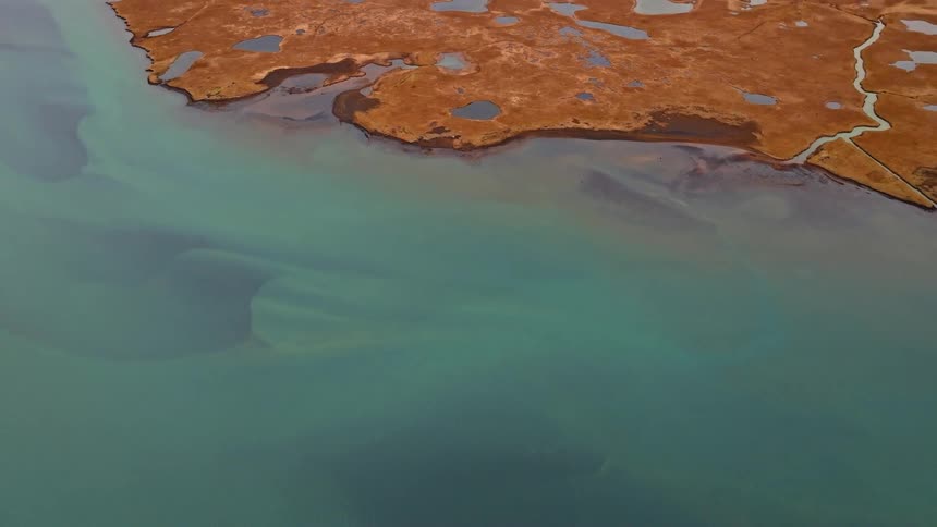 An aerial drone shot pulls back from beautiful turquoise glacial waters to reveal a vast brown and orange marshland landscape in Iceland