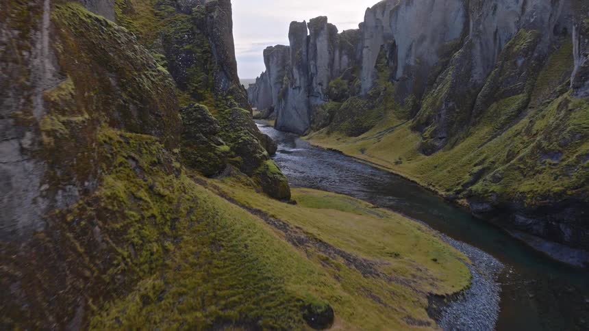 An epic aerial journey through a majestic and deep river canyon with steep, moss-covered cliffs in Iceland