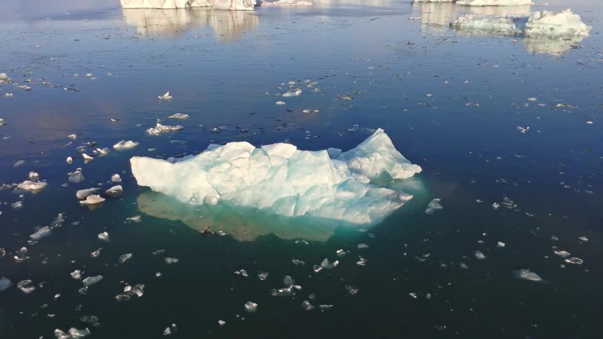An aerial view pulls back from a close-up of a blue iceberg to reveal the expansive Jökulsárlón glacier lagoon in Iceland