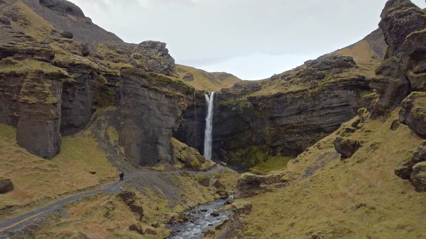 Aerial shot pulls back to reveal the stunning Kvernufoss waterfall nestled in a mossy canyon as hikers explore the scenic path in Iceland