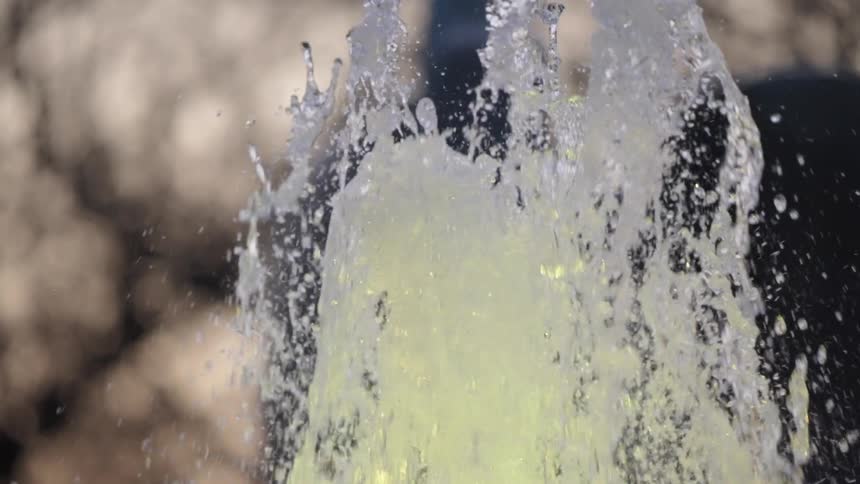 Slow motion close up of a beautiful fountain with green tinted water spraying upwards against a softly focused background