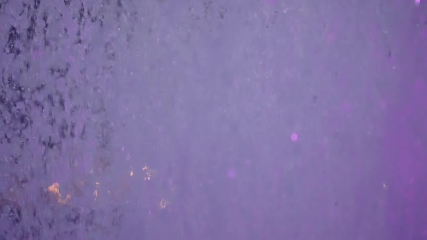 A mesmerizing slow-motion close-up of a purple fountain splashing against a dark background with bokeh city lights