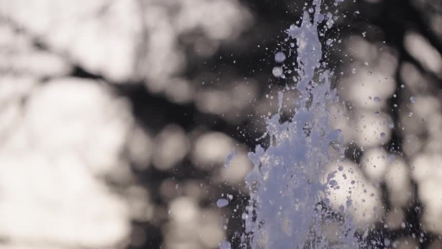 Water gracefully erupts from a fountain in a mesmerizing slow-motion close-up against a blurry, natural background