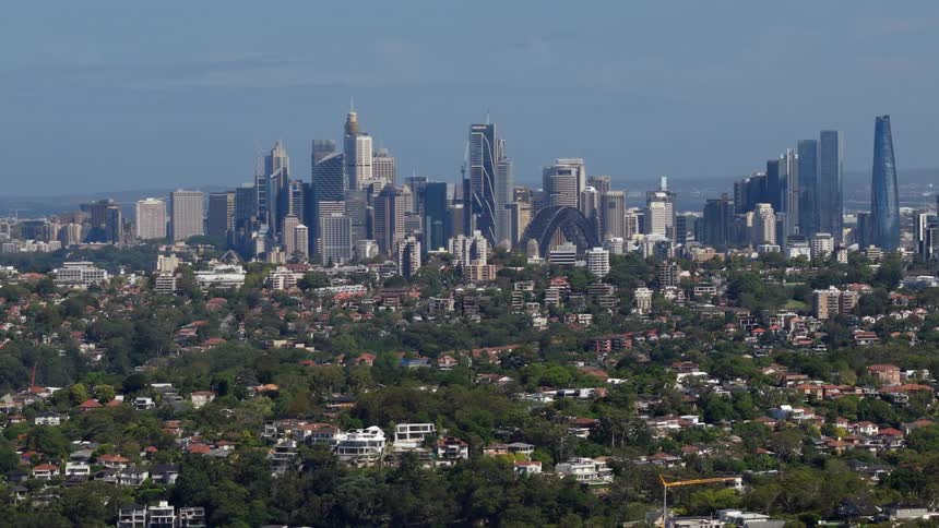 A panoramic view of the Sydney city skyline with the iconic Harbour Bridge rising above the lush green suburbs