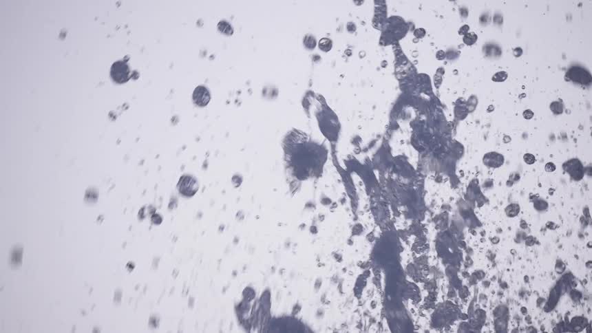 An artistic, abstract shot captures water from a fountain splashing upwards in super slow motion against a clean white background