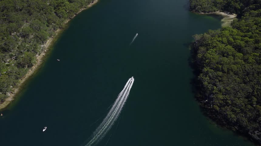 High aerial top-down view of speedboats cruising through a secluded river inlet surrounded by a dense forest