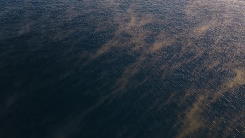 A static aerial view captures the serene and mesmerizing sight of golden mist evaporating from the deep blue ocean