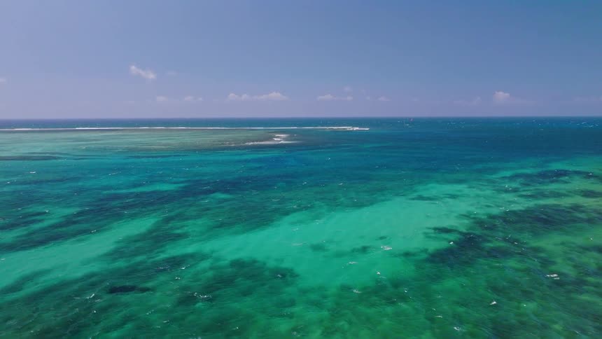 A serene aerial view of the vibrant turquoise and emerald waters of a tropical coral reef under a clear blue sky