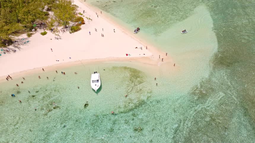 Top-down aerial view of a tropical sandbar where people swim in the clear turquoise water and a boat is anchored nearby