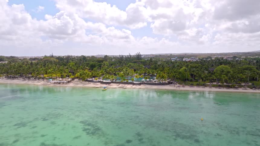 Drone flies backward from a woman on a tropical beach, revealing a stunning luxury resort and clear turquoise ocean