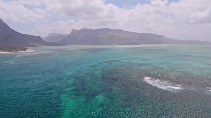 A stunning aerial view pans across the vibrant turquoise ocean and coral reefs to reveal the iconic Le Morne Brabant mountain in Mauritius