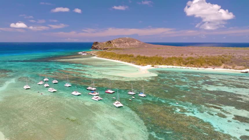 Ascending aerial view of sailboats and catamarans anchored in a stunning turquoise lagoon by a tropical island