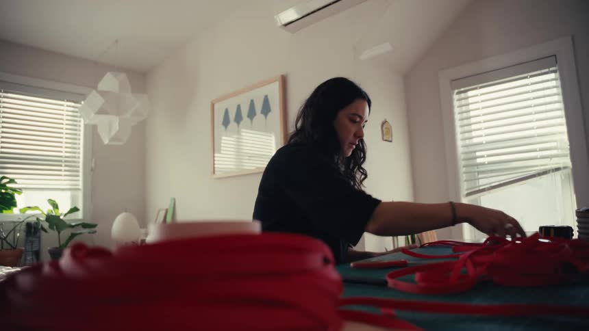 Low angle slow motion shot of a focused female artisan measuring a long red strap at her work table in a bright studio