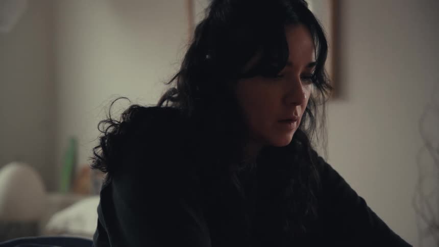 A young woman with dark wavy hair concentrates intently while working in a softly lit room