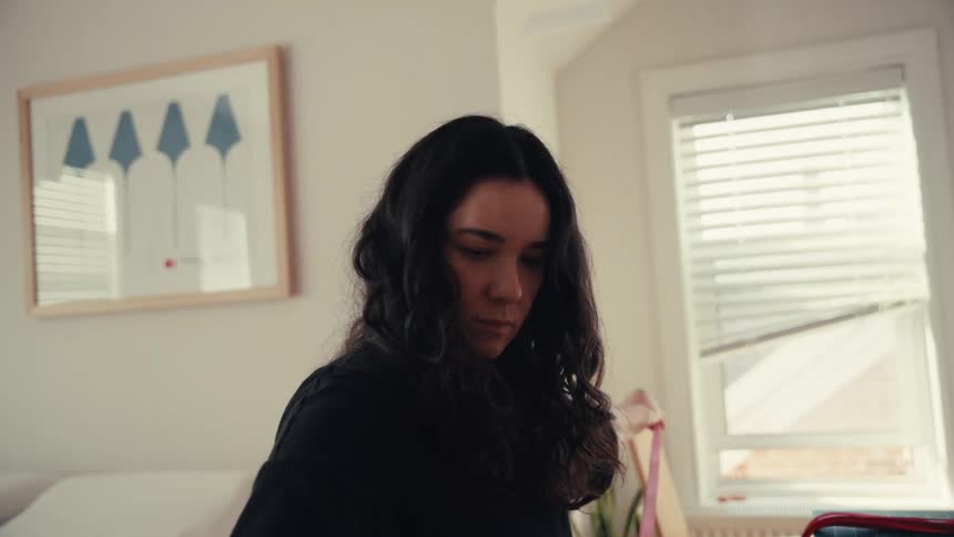 A focused woman with dark wavy hair carefully measures a piece of red string in a sunlit room