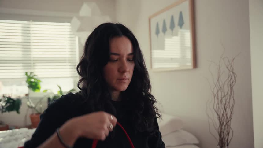 A young woman with dark hair carefully winds a long red ribbon around her hands in slow motion