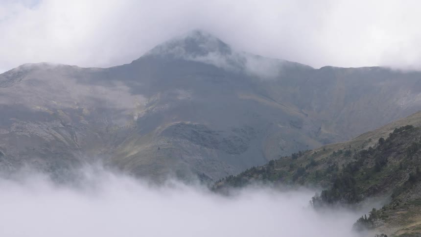 Majestic mountain peak rises above a thick blanket of fog and clouds in a serene, static shot