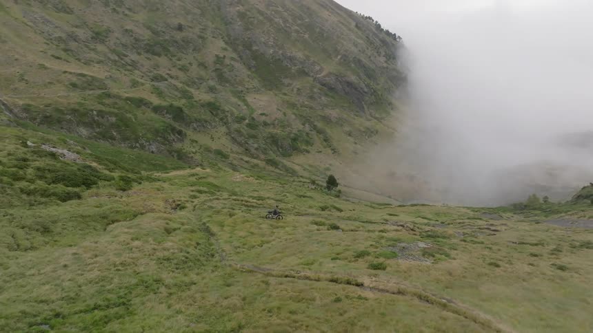 Dramatic aerial reveals a lone mountain biker on a high alpine trail overlooking a spectacular sea of clouds filling the valley below
