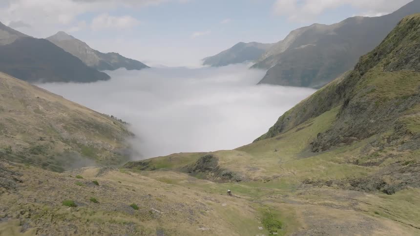 An epic aerial view flies forward over a vast mountain landscape towards a stunning valley filled with a sea of clouds