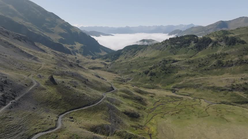 A majestic static aerial view of a vast mountain valley with a winding road leading towards a beautiful sea of clouds in the distance