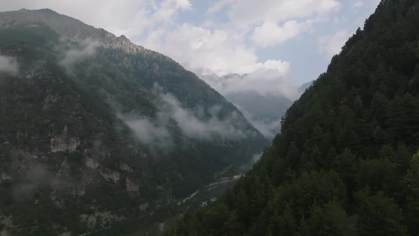 Aerial footage slowly reveals a vast, misty mountain valley covered in dense evergreen forests