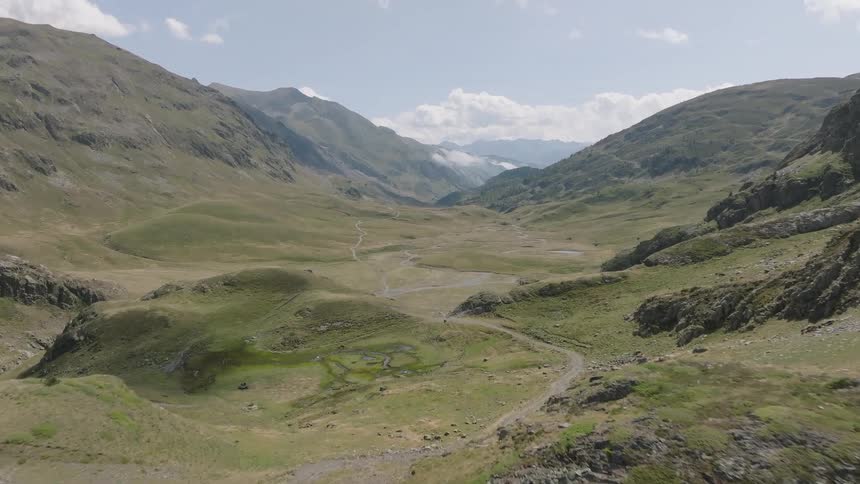 An aerial view shows a lone mountain biker riding through a vast, beautiful green mountain valley on a sunny day