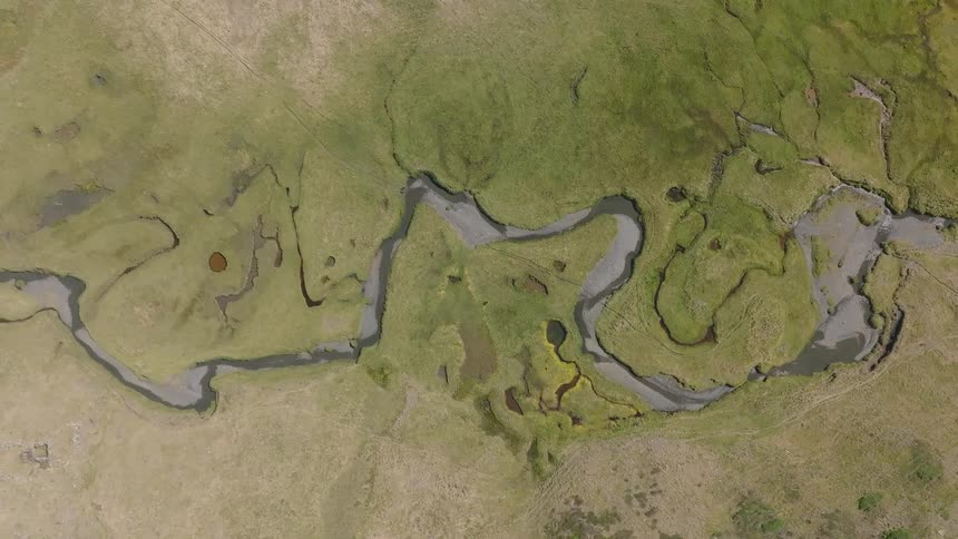 Top-down drone footage shows a winding river carving through a verdant, mossy landscape