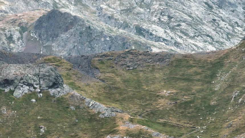 A group of hikers trek along a winding path through the vast and rugged Pyrenees mountains as the camera slowly zooms out