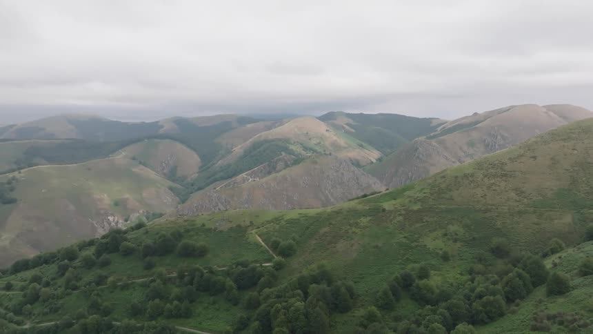A serene, static aerial view of a vast, rolling green mountain range under a cloudy sky