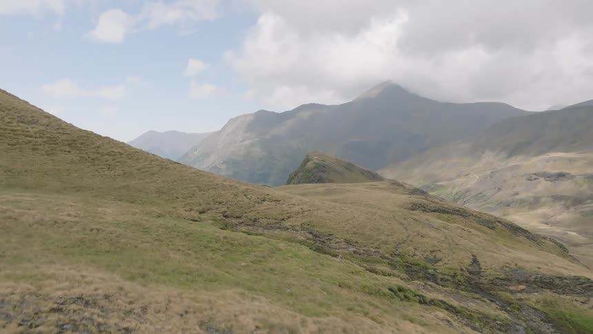 Aerial view following a mountain biker along a remote ridge trail, revealing a stunning mountain landscape with a lake and valley filled with clouds