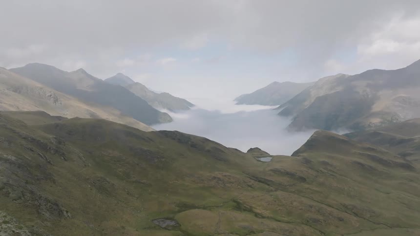 A stunning aerial view flies over a misty mountain ridge to reveal a vast valley completely filled with a sea of clouds