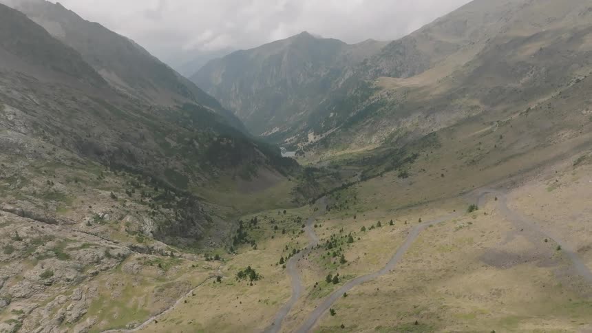 Slow aerial flight over a winding road through a vast and remote mountain valley leading towards a distant lake