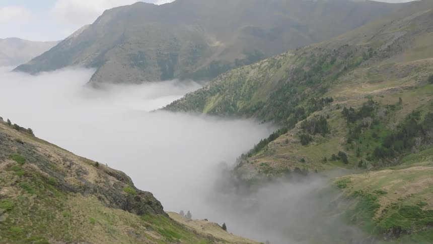 A majestic aerial view follows a lone hiker on a remote mountain trail, ascending to reveal an epic panorama of peaks rising above a sea of clouds