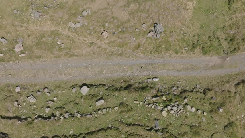 Static aerial top-down view of a mountain biker riding on a gravel path through a rocky, grassy landscape