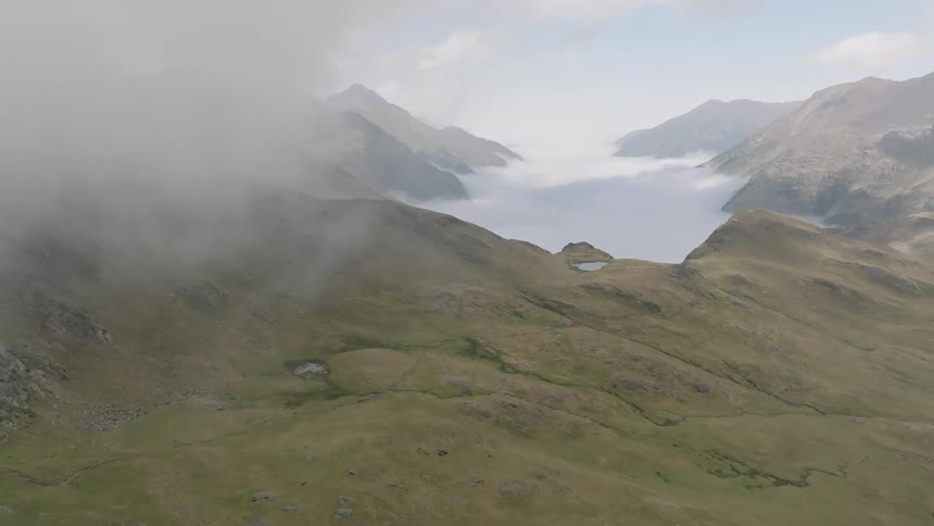 Aerial flight over a rocky mountain ridge reveals a majestic sea of clouds filling the valley below