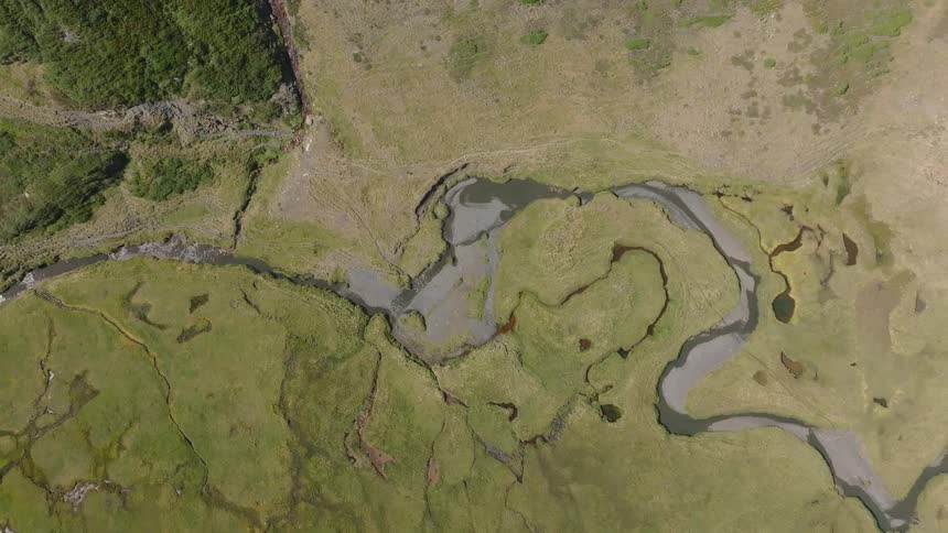 An abstract top-down aerial view slowly pans over an intricate meandering river snaking through a lush green valley