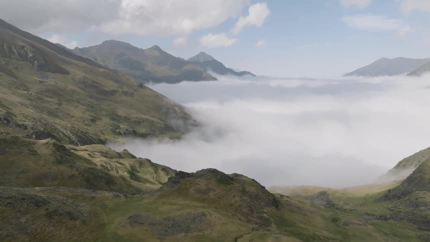 An epic aerial view pulls back over a vast mountain range, revealing a serene sea of clouds filling the valley below