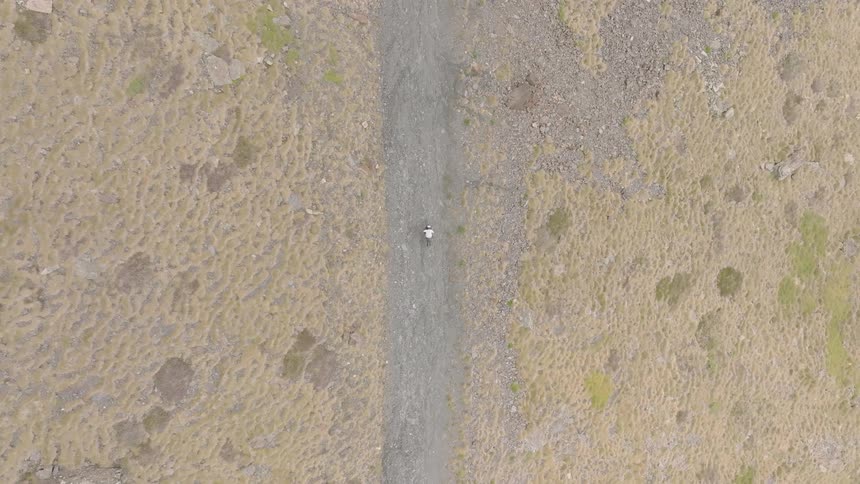 Aerial top-down view of a lone hiker walking along a rugged trail on a grassy mountainside