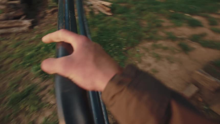A first-person perspective of a farmer opening a metal gate and walking into a field while carrying a chicken waterer