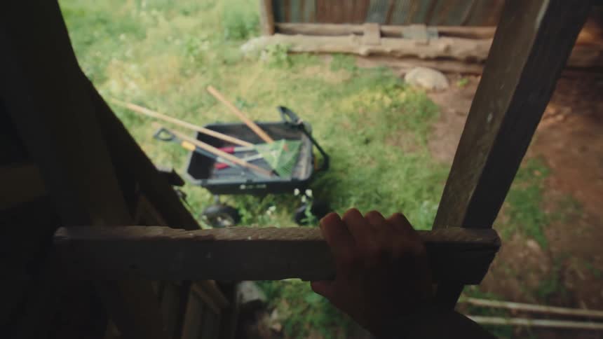 A first-person point of view of a person carefully climbing down a rustic wooden ladder in a barn