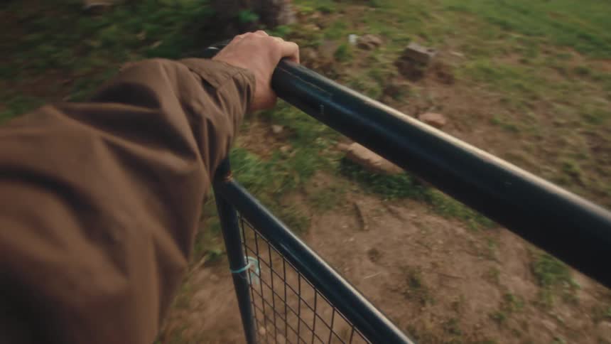 A first-person view of a hand opening a rustic metal gate and entering a grassy pasture at golden hour