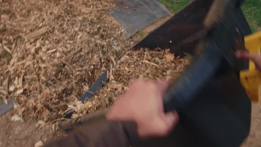 First-person point of view of a gardener dumping a wheelbarrow full of wood chip mulch in a backyard garden