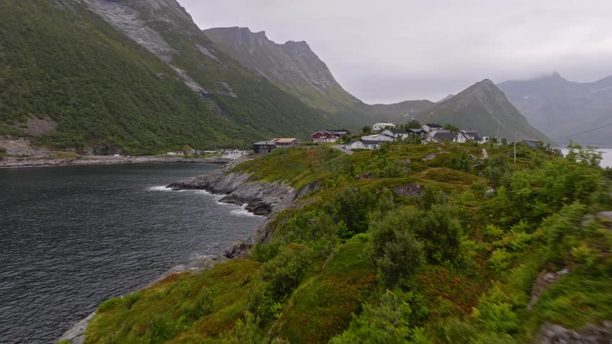 An aerial journey over a scenic Norwegian fjord reveals a charming village nestled between the water and towering mountains