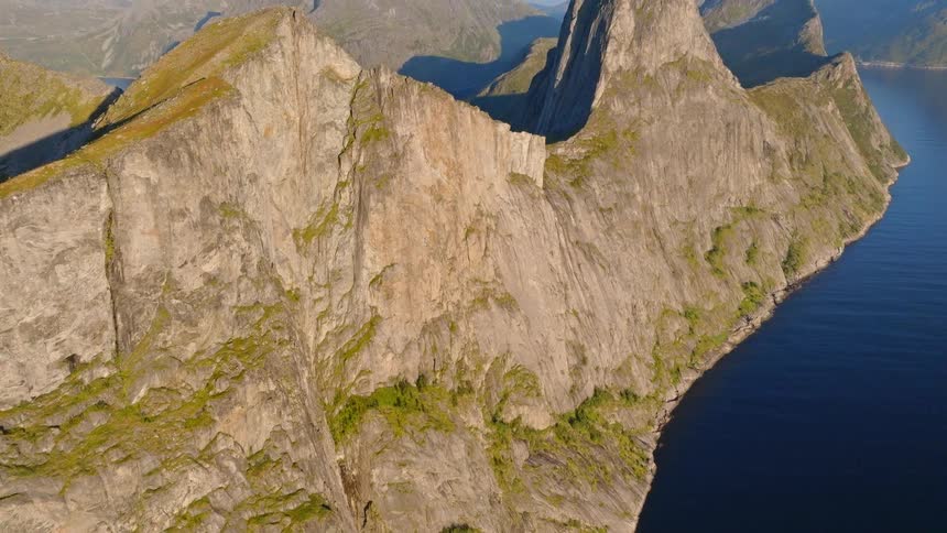 A cinematic aerial reveal of a majestic and rugged mountain range rising from the deep blue sea along a stunning coastline
