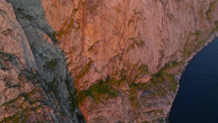 A top-down aerial view tilts up to reveal a stunning mountain range along the coast of Norway during sunset